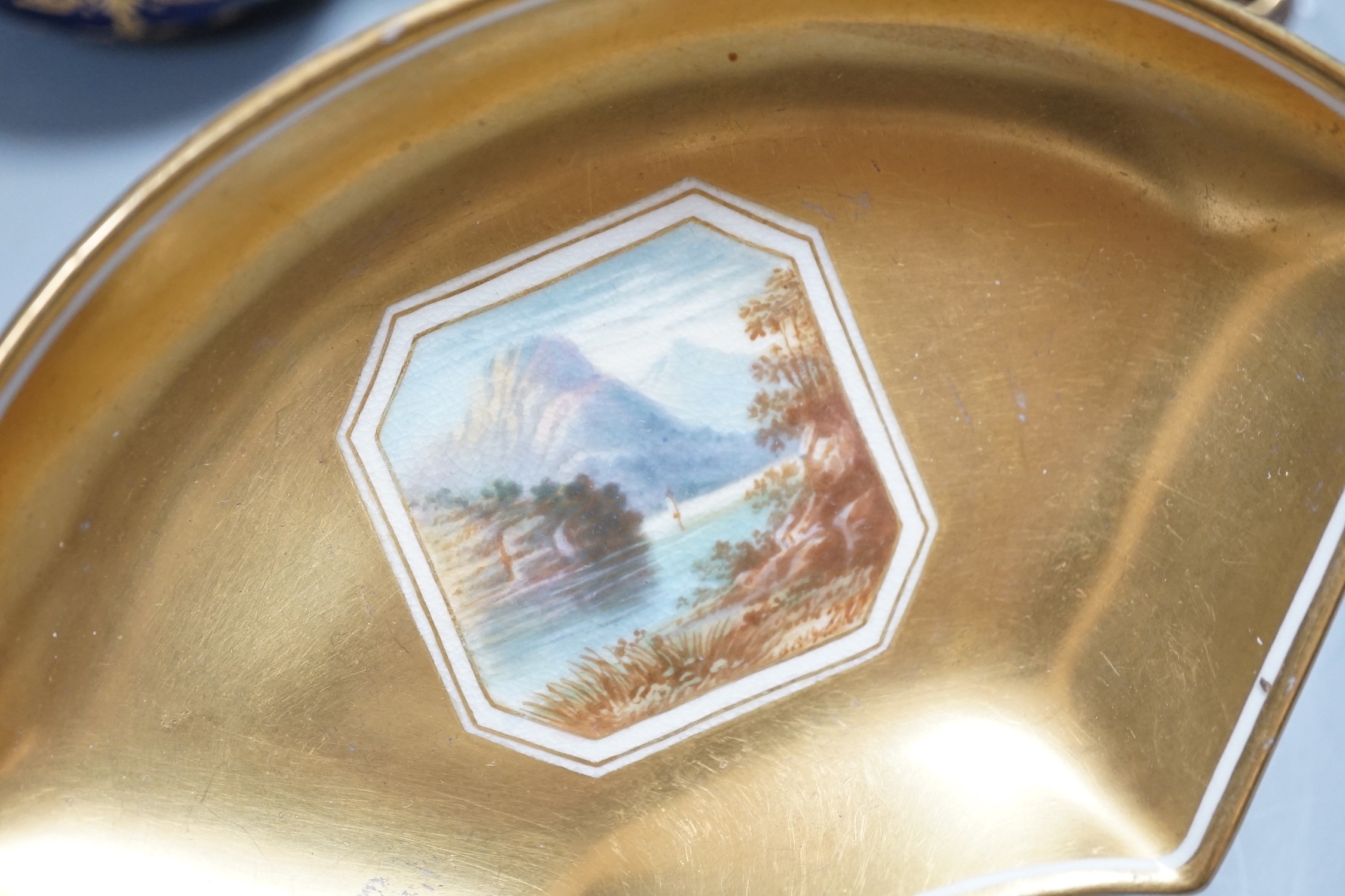 A 19th century Coalport fan shaped dish painted with a Loch scene, two small cup with twin handles decorated with raised gilding on a cobalt blue ground with crown marks, a Copeland jewelled cup and saucer with blue grou